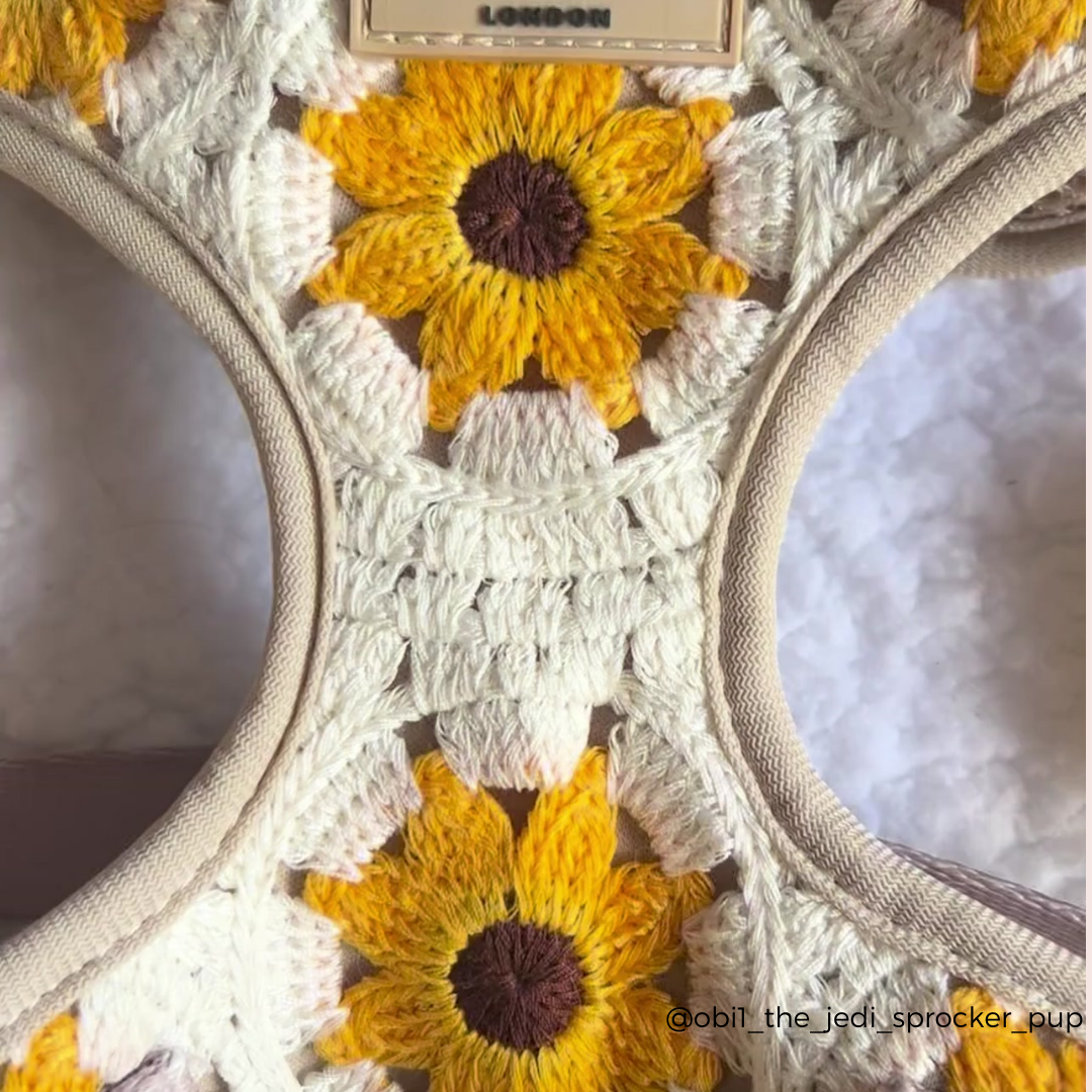 A close-up of a crochet pattern showcasing vibrant yellow sunflowers with brown centers. The intricate design, framed by beige stitching, evokes the charm of Cocopup London's Sunflower Patch Adjustable Neck Harness, Lead & Collar Bundle. A small tag reading "London" is visible at the top, with the Instagram handle "@obi1_the_jedi_sprocker_pup" noted at the bottom right.