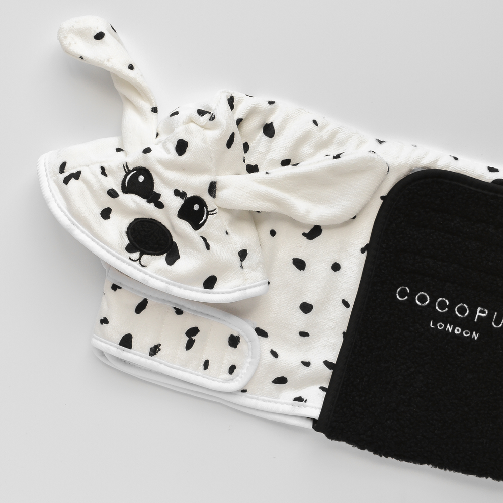 A neatly folded black and white spotted, dog-themed garment featuring floppy ears and a cute face lies next to a premium microfibre Dalmatian Drying Robe by Cocopup London. The vivid details stand out beautifully against the white background.