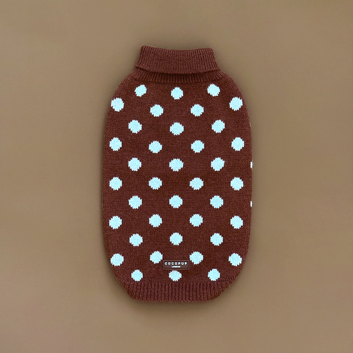 A brown knit dog jumper with pale blue polka dots, on a solid beige background.