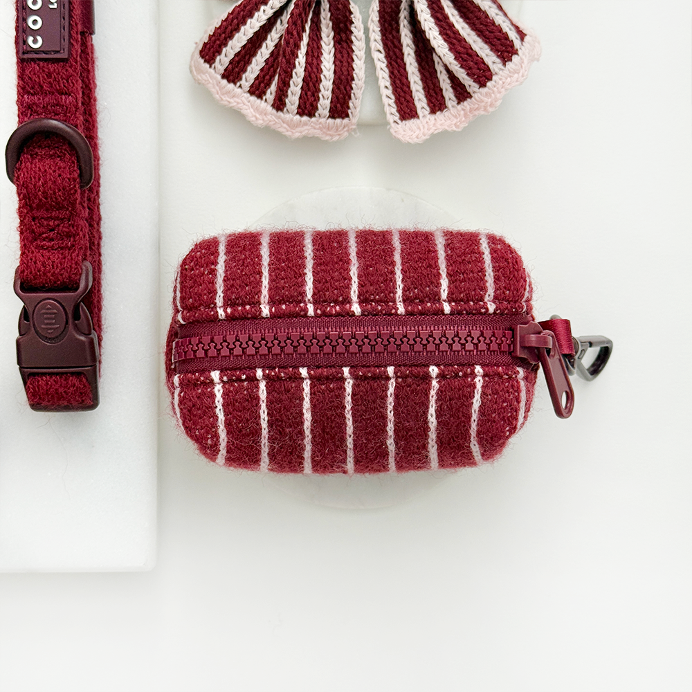 Knitted dog poop bag dispenser with burgundy and baby pink vertical stripes and a colour matched zip closure.