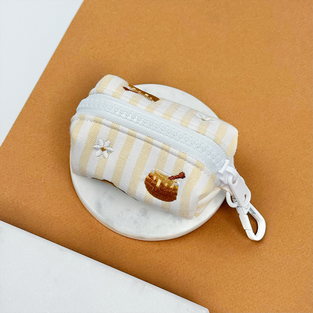 Pale yellow and white striped poop bag holder with embroidered honeycomb and bees.