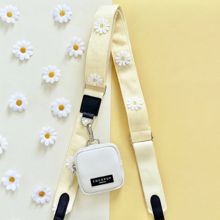 Oyster white dog walking bag with daisy accents and attached treat pouch, displayed alongside fresh daisies.