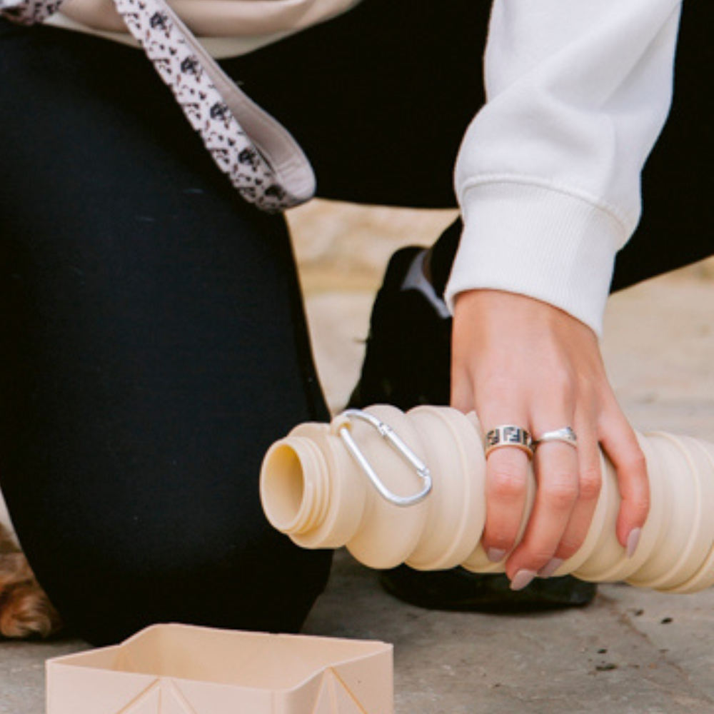 Model pouring water from the Cocopup Nude Collapsible Water Bottle into the Cocopup Nude Foldable Travel Bowl.